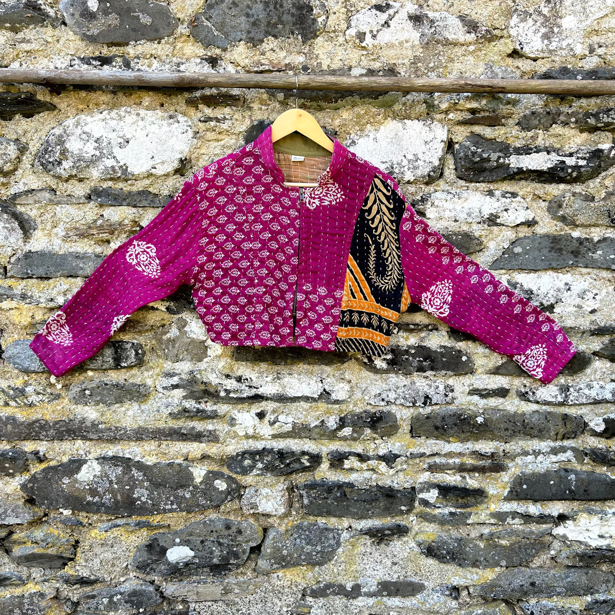 Pink Gudri kantha jacket made from reclaimed cotton with contrasting patterned panel, shown hanging against a stone wall